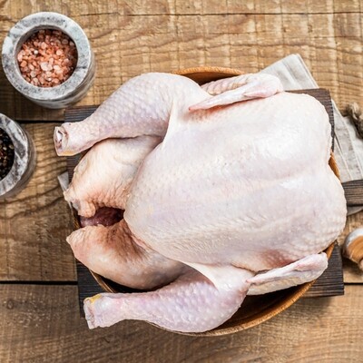 Whole Chicken Freezer Clean Out: Raw, pale pink chicken on a wooden cutting board with salt, pepper, & garlic cloves.