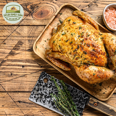 Golden roasted BIG Chicken Roaster Special on wooden tray, seasoned with herbs, next to cleaver and pink salt.