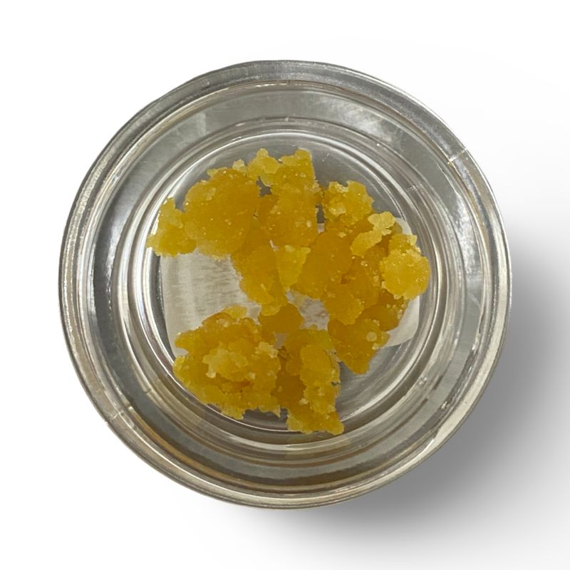 Top-down view of Mirage Cake Crumble in a glass jar showing golden, fluffy cannabis concentrate