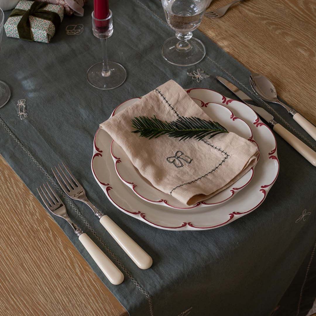 Rustic linen napkin with embroidered bow and stitched trim—adds charm to Christmas place settings.