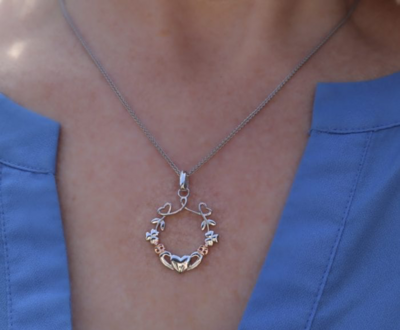 Sterling silver pendant featuring Irish Shamrock, Claddagh, and heart symbols, celebrating Irish heritage. Shown on model. 