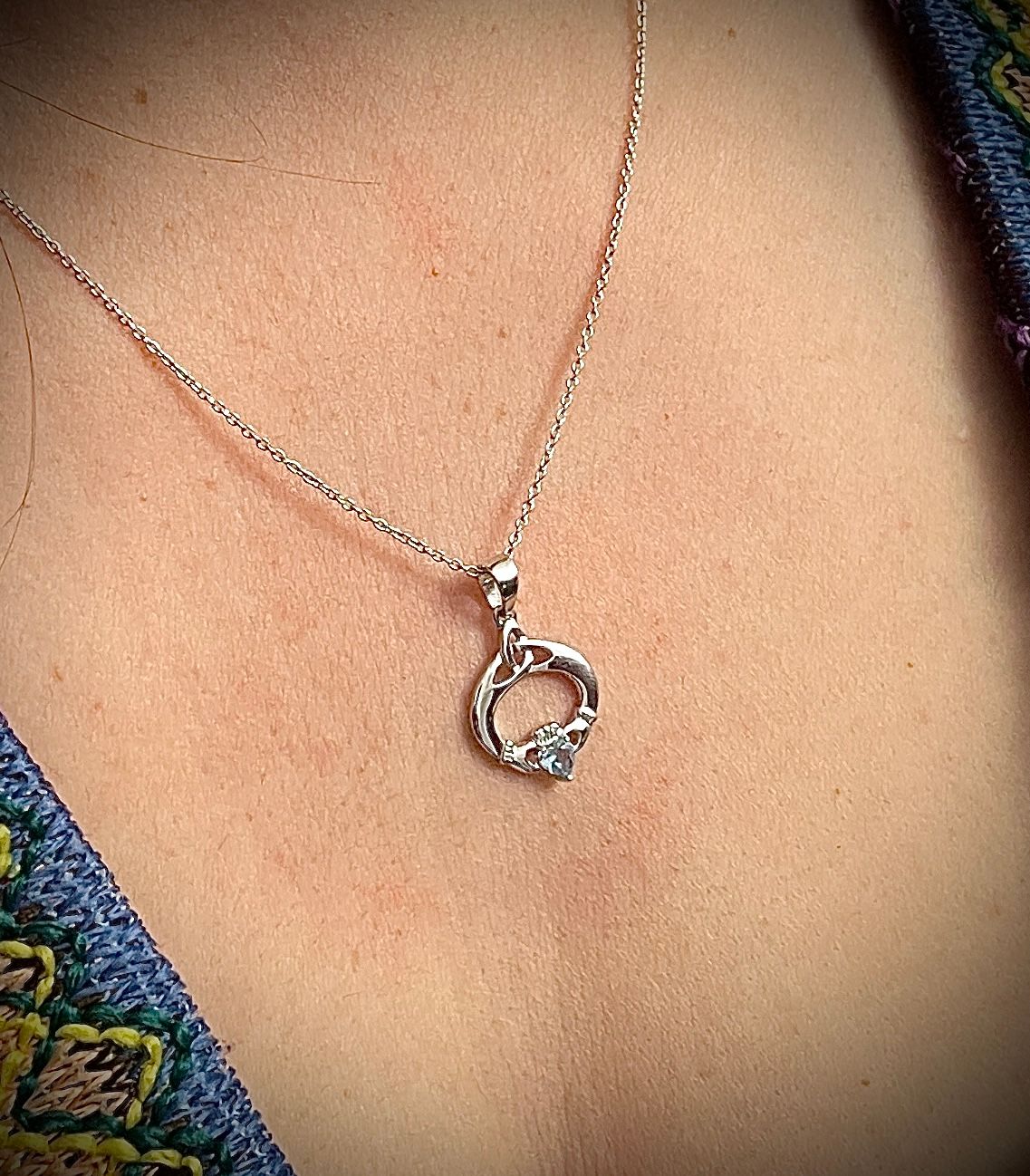 Irish-inspired sterling silver Claddagh necklace featuring a colored gemstone, celebrating Irish heritage, worn by model. 