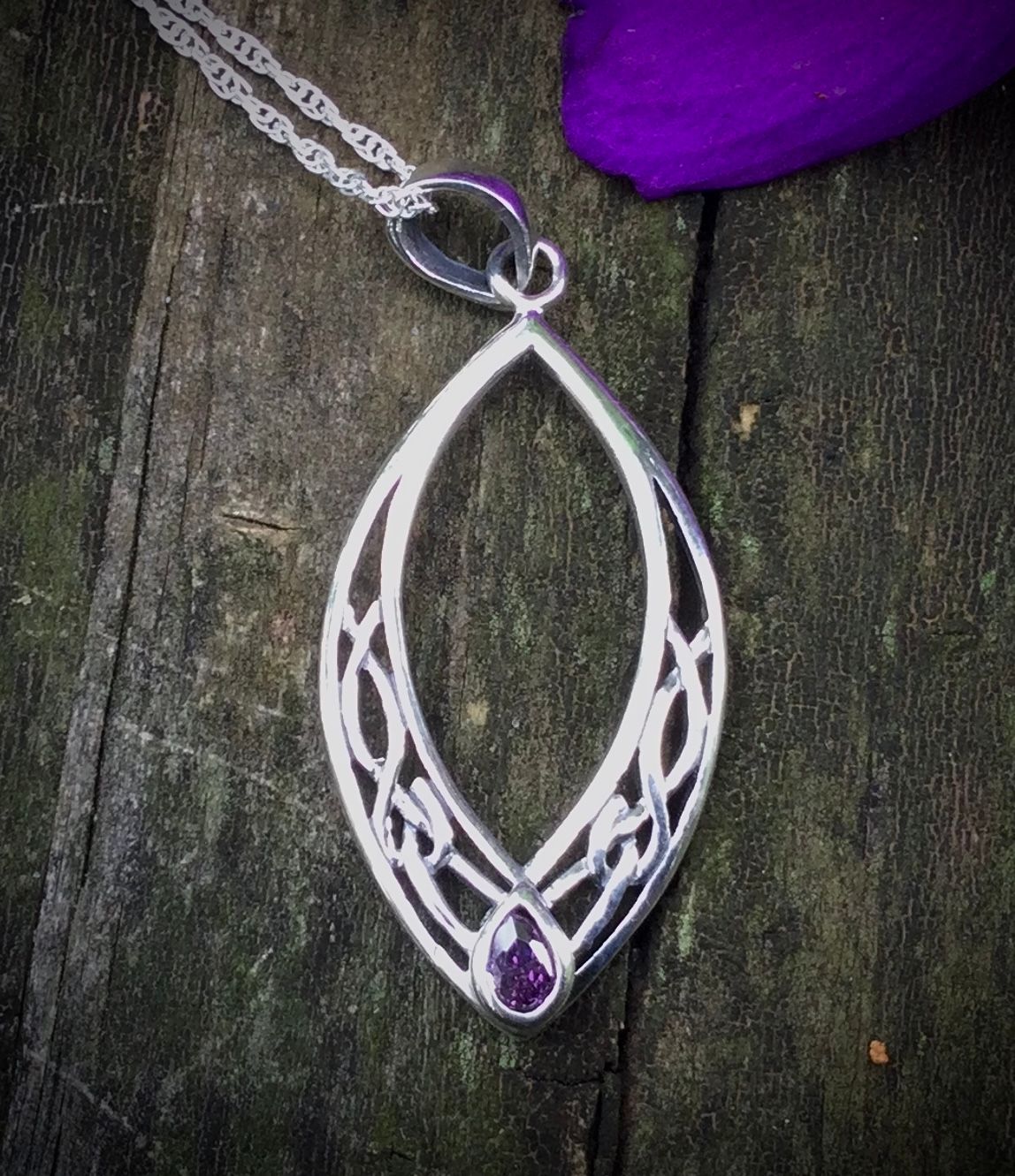 Oval Silver Pendant with Amethyst Colored Stone Sterling silver oval Celtic knot pendant on bark with an amethyst-colored gemstone.