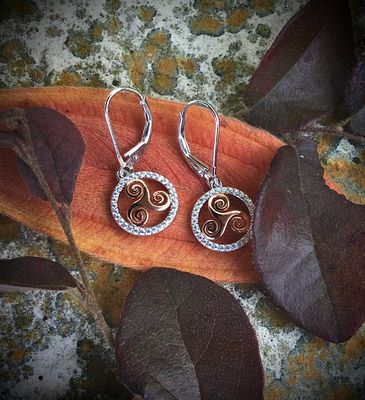 Sterling silver gold-plated Celtic triskele earrings, handcrafted Irish jewelry, on orange leaf.