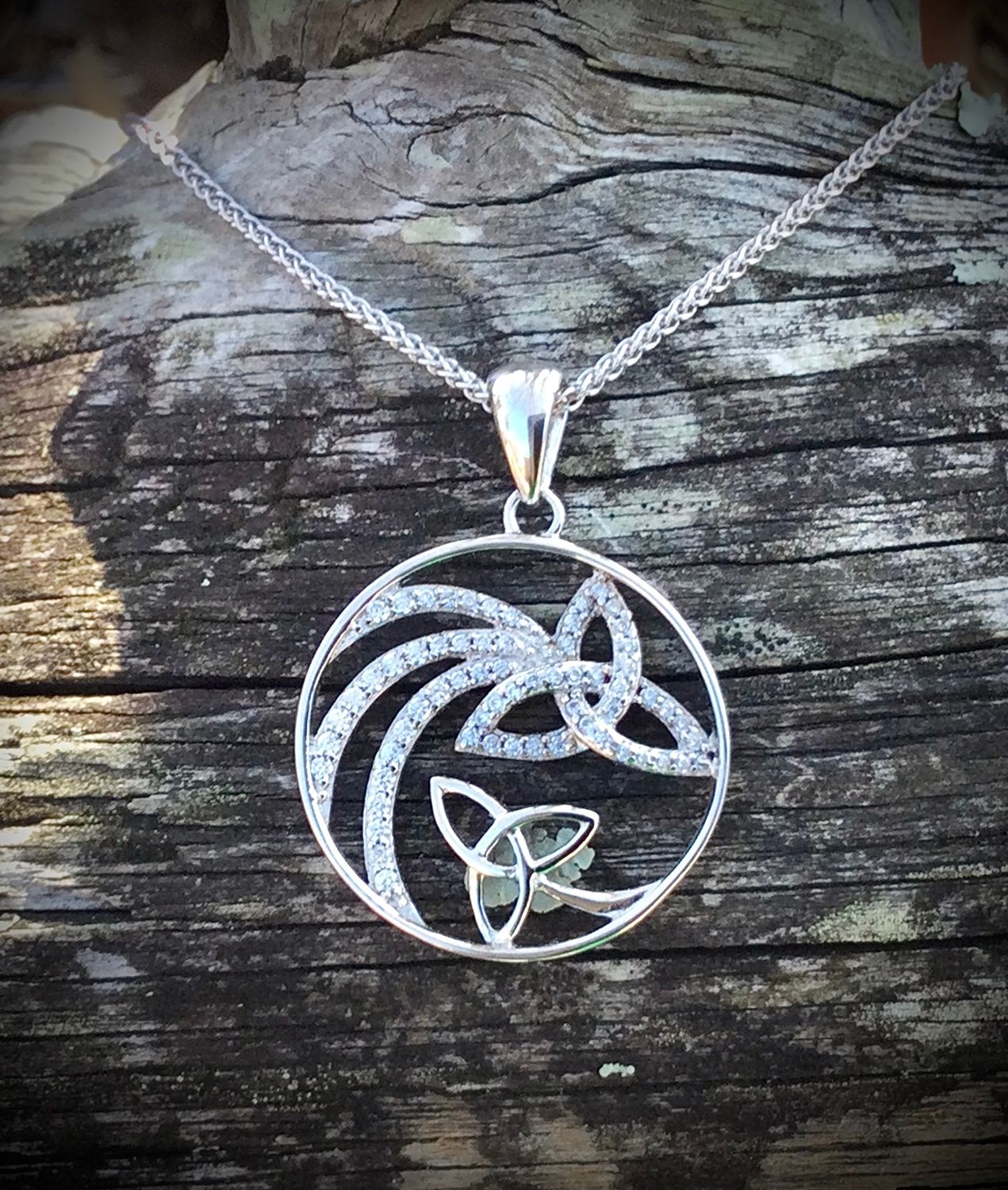 Sterling silver shooting star pendant with sparkling CZ stones and trinity knot, celebrating Celtic heritage, on bark. 