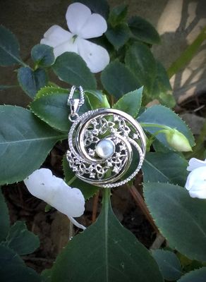 Irish-inspired sterling silver pendant with Celtic knot design and central Mother of Pearl gemstone, shown near plants. 