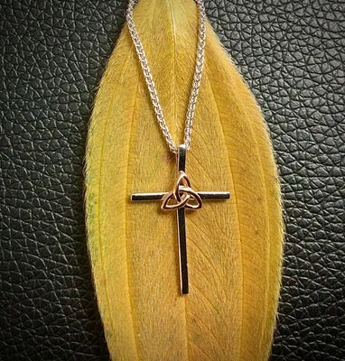 Sterling silver Celtic cross pendant with a central rose gold plated Trinity knot, inspired by Irish heritage, shown on leaf.