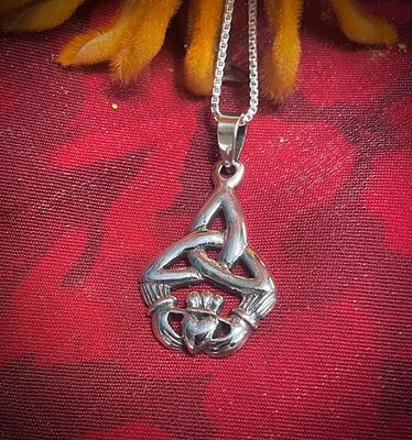 Sterling silver pendant featuring a Trinity Knot and Irish Claddagh design, celebrating Celtic culture, on red fabric. 