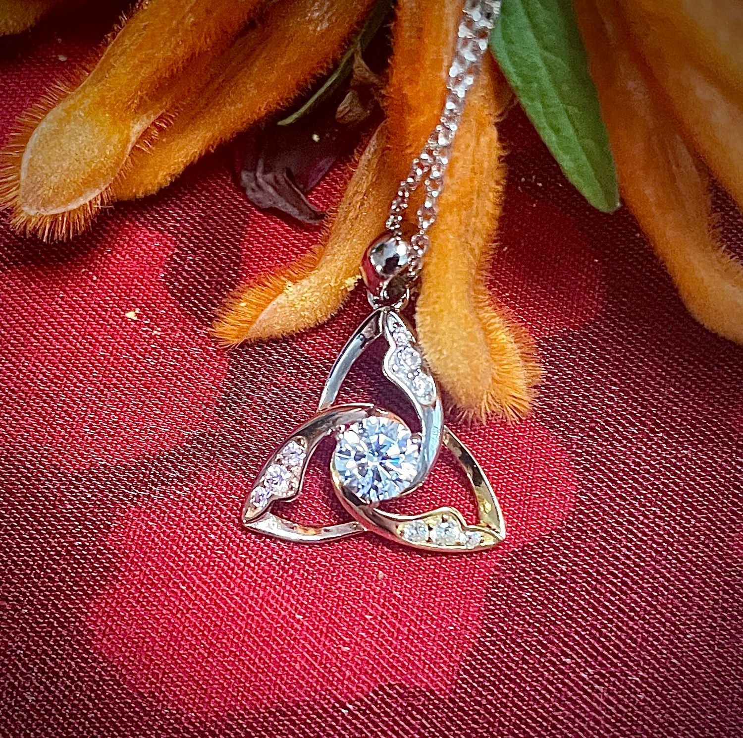 Sterling silver Celtic Trinity Knot necklace with tri-color gold plating and sparkling CZ centerpiece, shown on red fabric. 