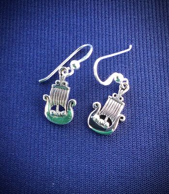 Detailed Celtic Viking Ship drop earrings in polished sterling silver, showcased on blue fabric. 