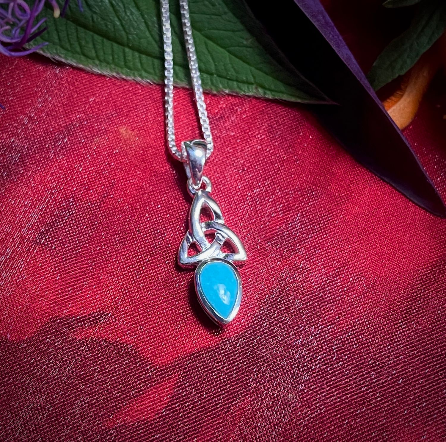 Trinity Knot with Aquamarine Stone Handcrafted Celtic Trinity Knot pendant on red fabric with aquamarine stone.