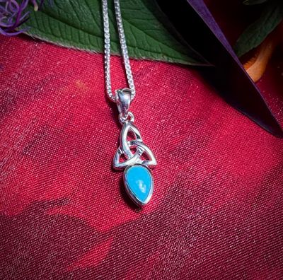 Handcrafted Celtic Trinity Knot pendant on red fabric with aquamarine stone.