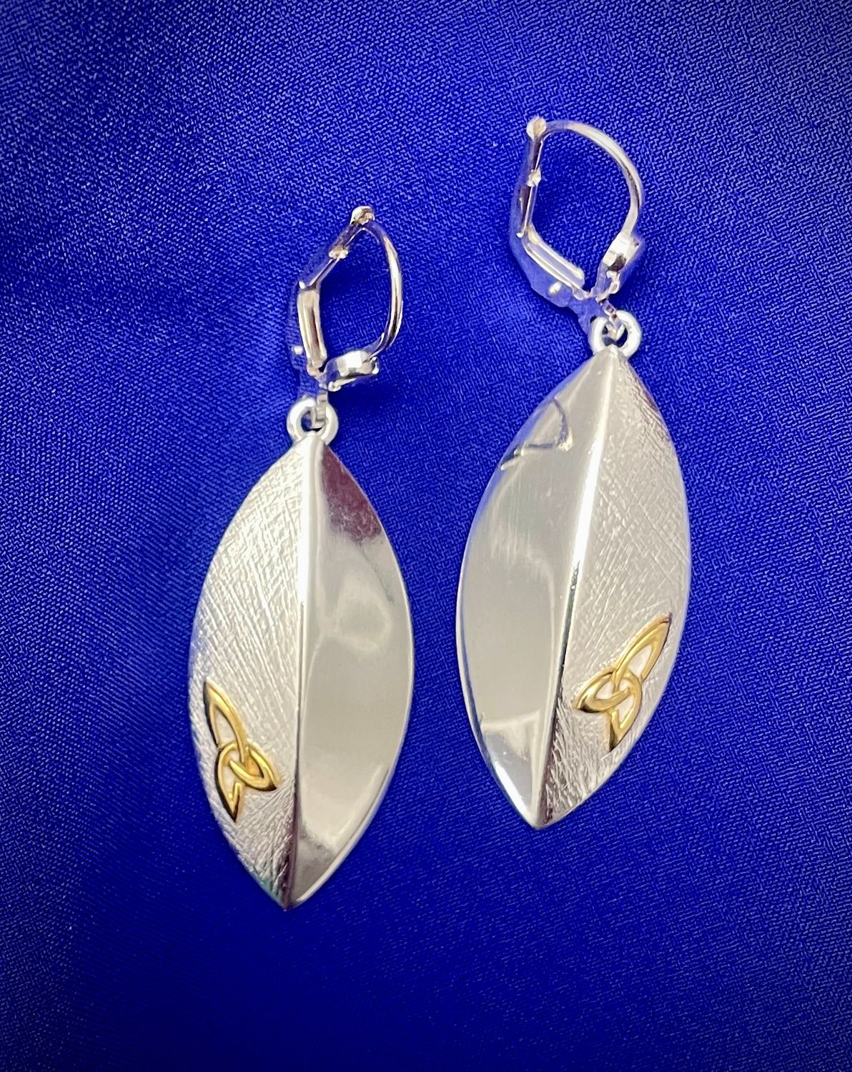 Handcrafted silver shield earrings with intricate raised Trinity Knot detailing, inspired by Celtic heritage.