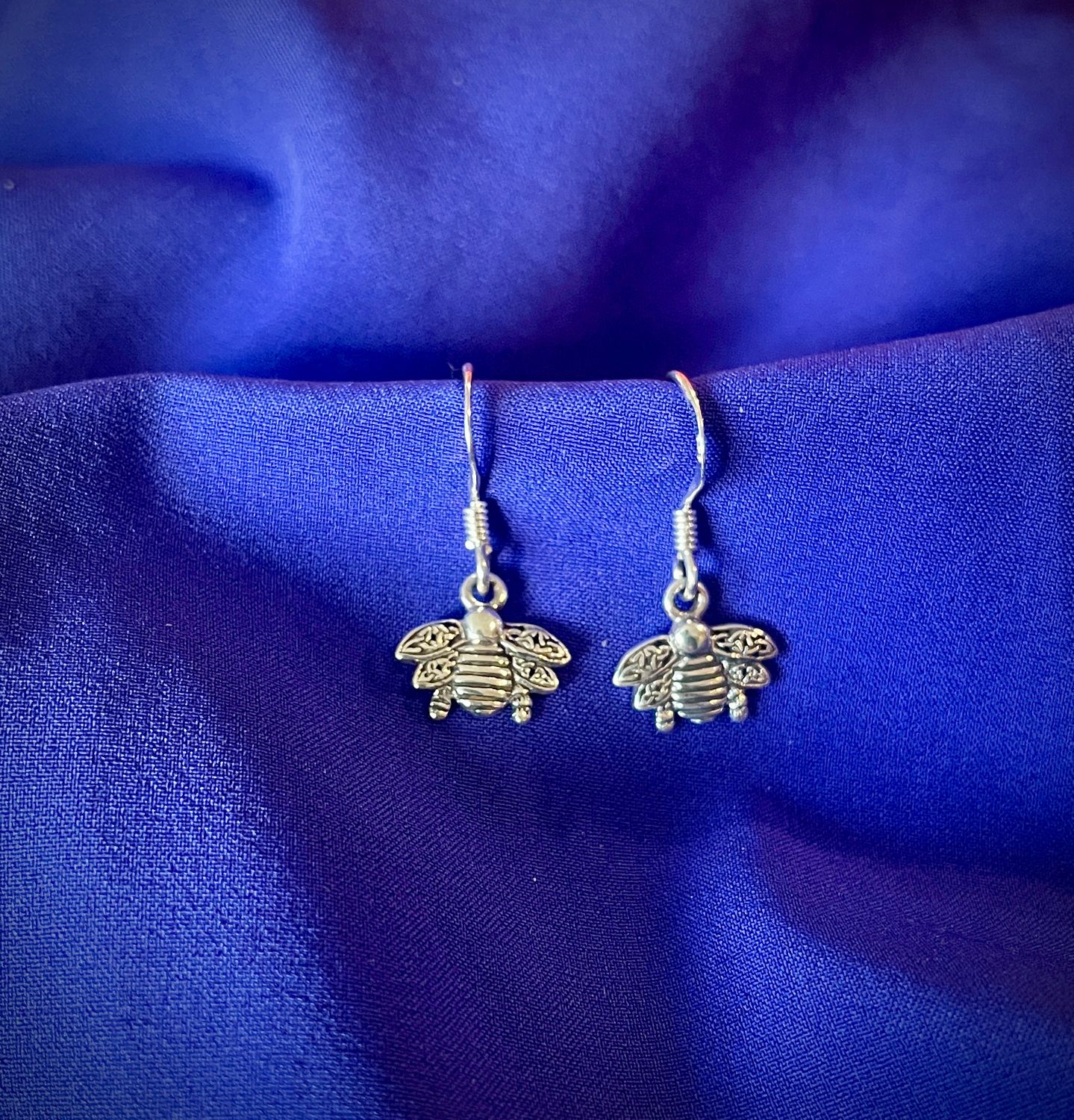 Irish Celtic bee earrings in sterling silver, inspired by Outlander and Celtic traditions, shown on purple fabric.