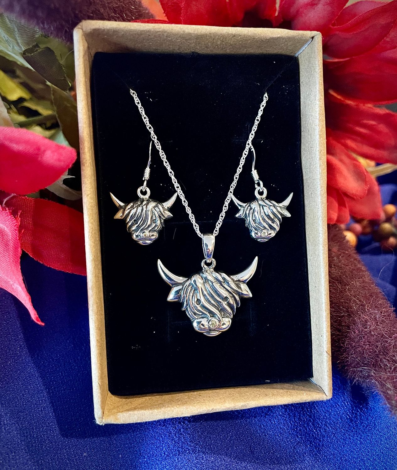 Sterling Silver Scottish handcrafted Highland cow earrings and pendant jewelry set, shown in jewelry box by flowers. 