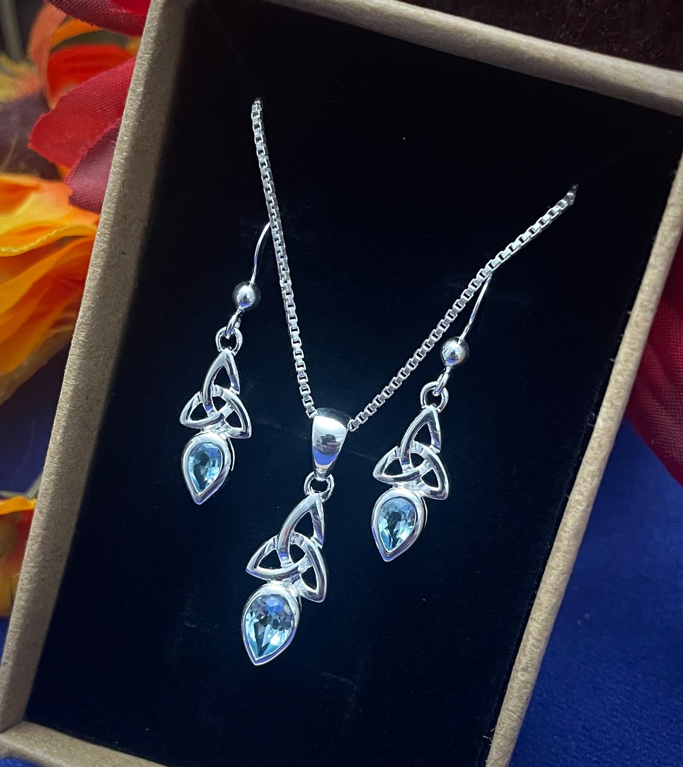 Silver Celtic Trinity Knot pendant and earrings with blue topaz gemstone, meaningful birthstone jewelry, in jewelry box.