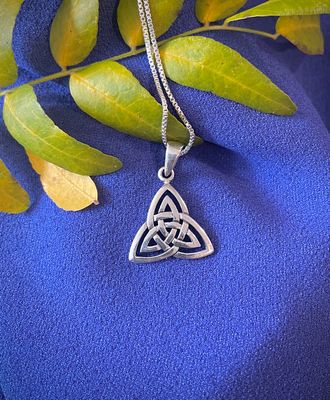 Elegant sterling silver triquetra pendant on sterling silver chain, symbolizing unity and eternity, shown on blue fabric.