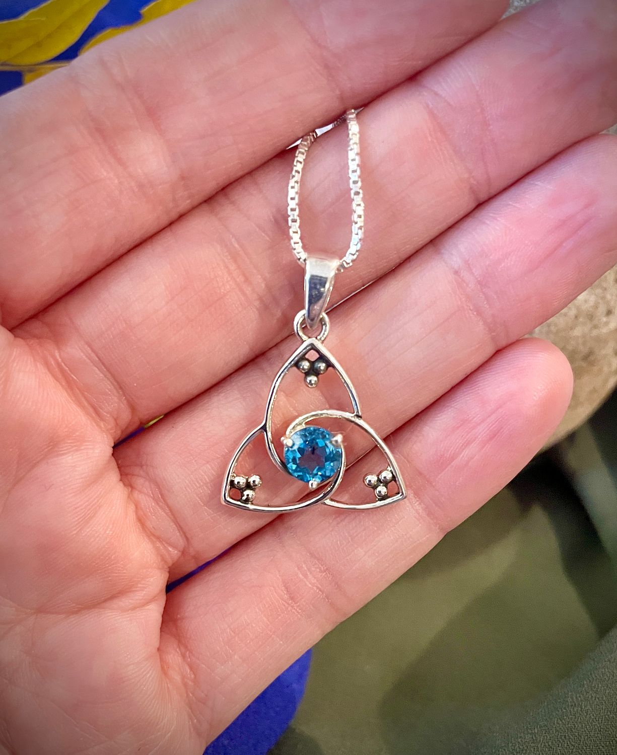 Sterling silver Celtic Trinity Knot pendant with blue sapphire, handcrafted Irish jewelry gift for her. Held by model.