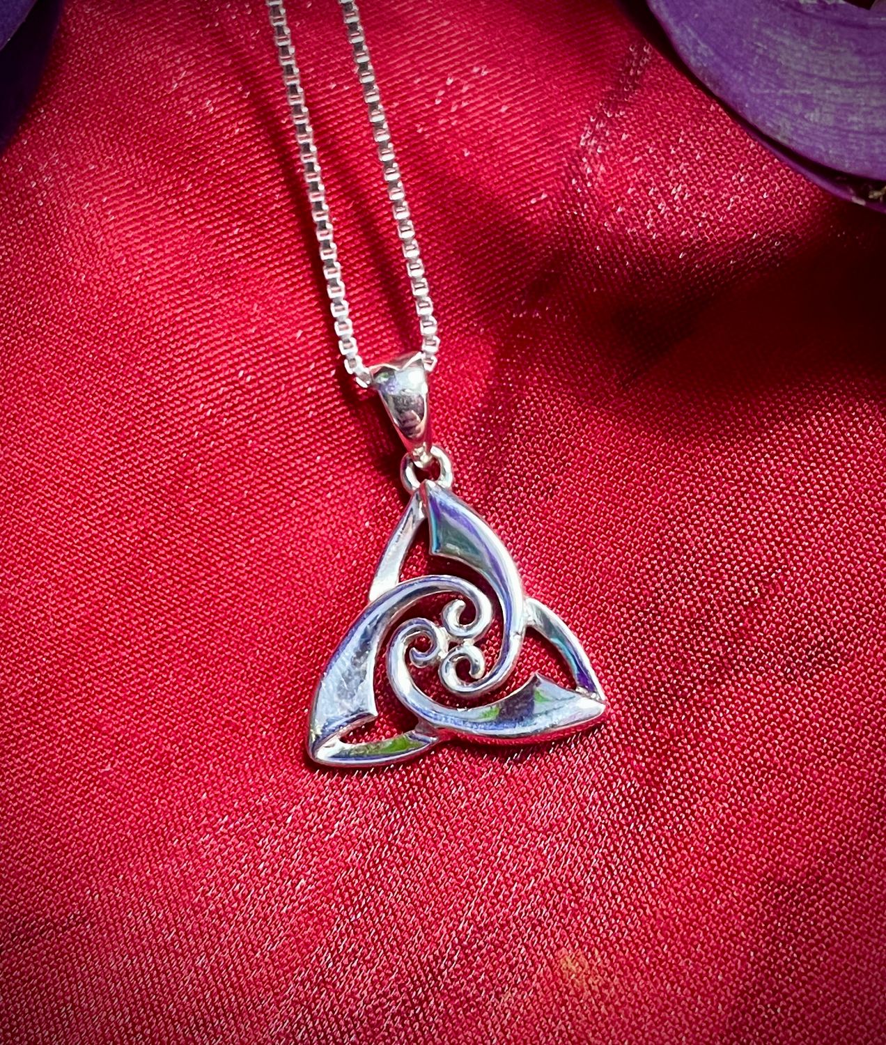 Sterling Silver Trinity Swirl Knot Pendant Sterling silver Celtic Trinity Knot pendant with swirl design, handcrafted Celtic jewelry shown on red fabric.