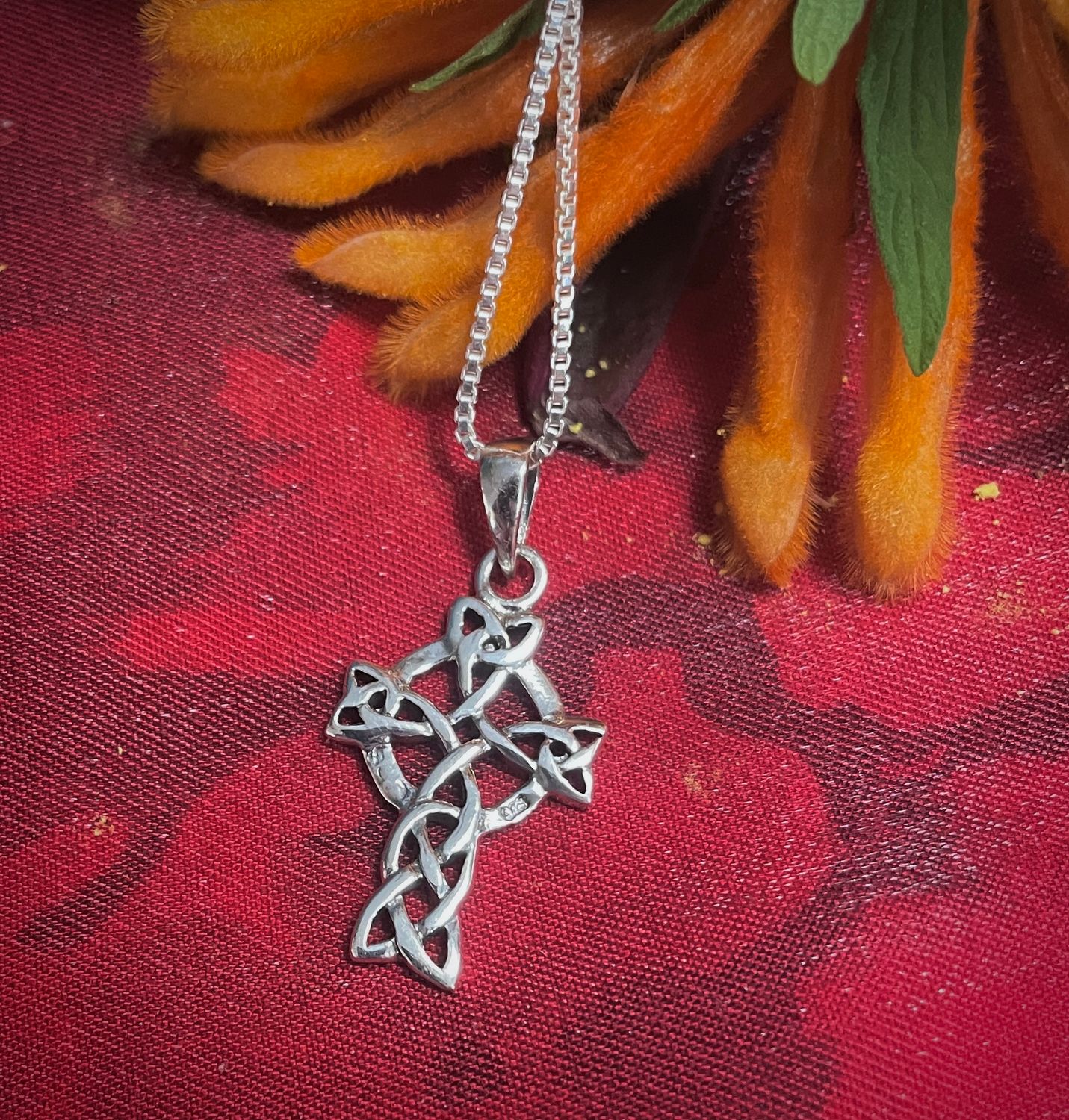 Sterling silver Celtic cross pendant with trinity knots and intricate Celtic knot detailing, heritage jewelry on red fabric.