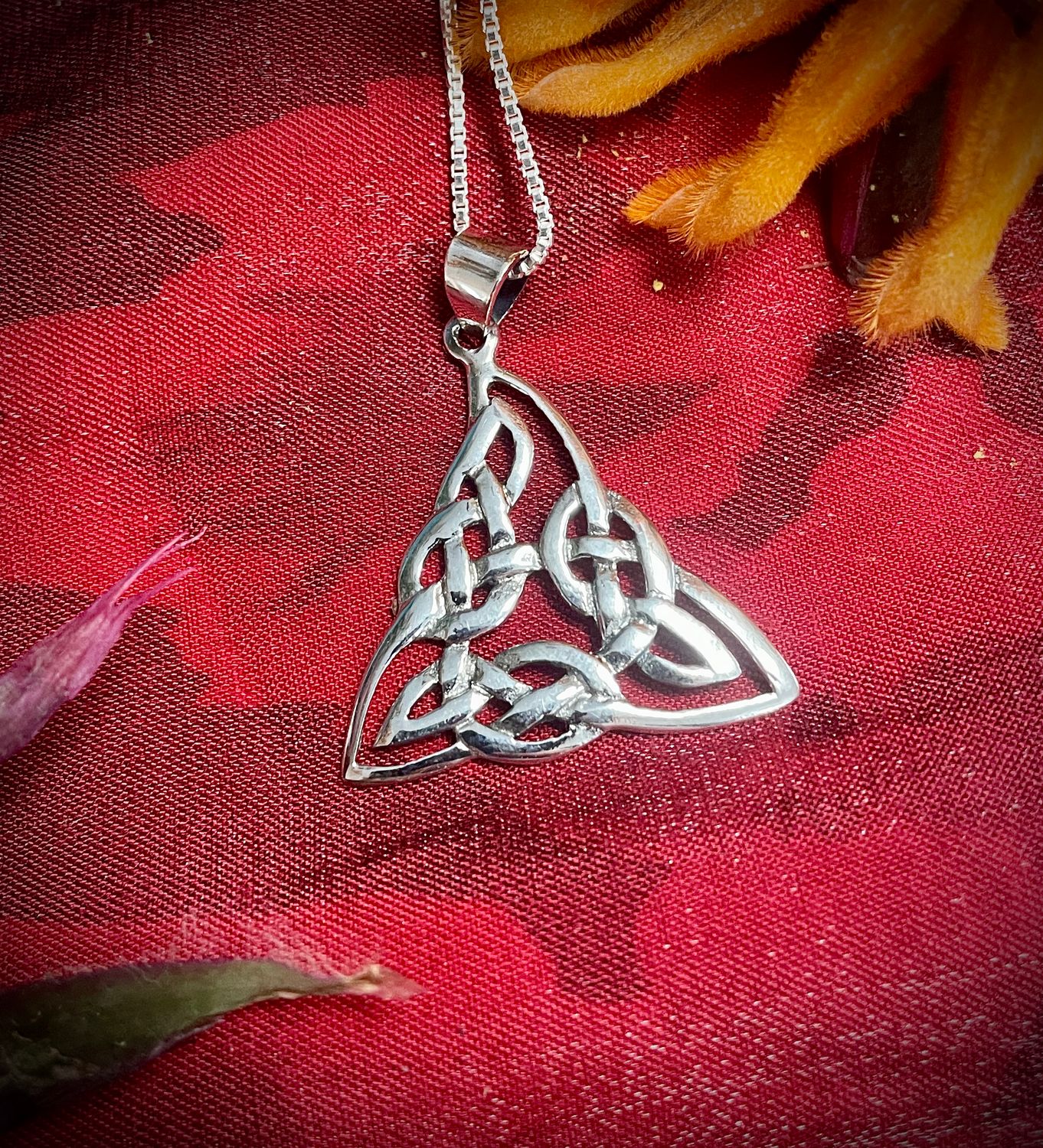 Sterling silver triquetra pendant necklace with intricate Celtic knot design, on red fabric.
