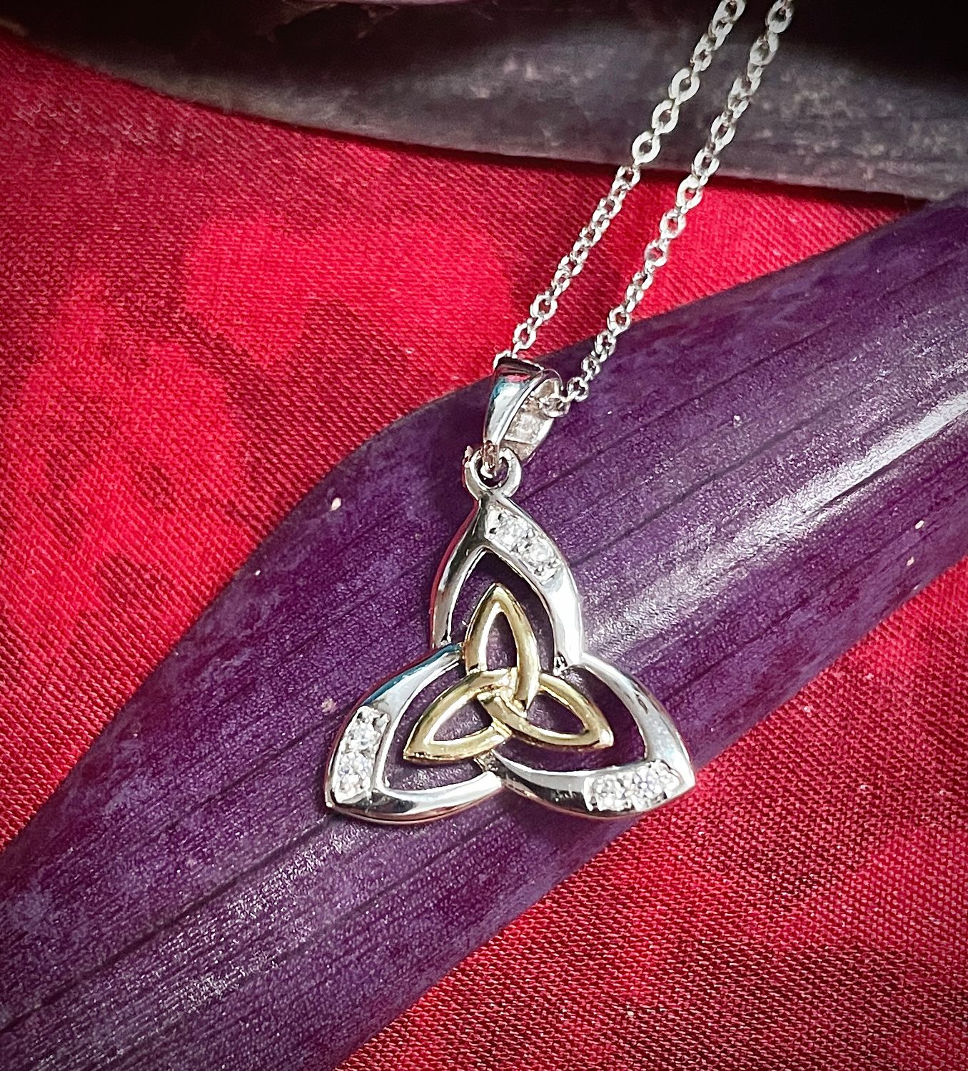 Sterling silver Trinity Knot pendant with yellow gold plating, Celtic design and heritage jewelry, on purple leaf. 