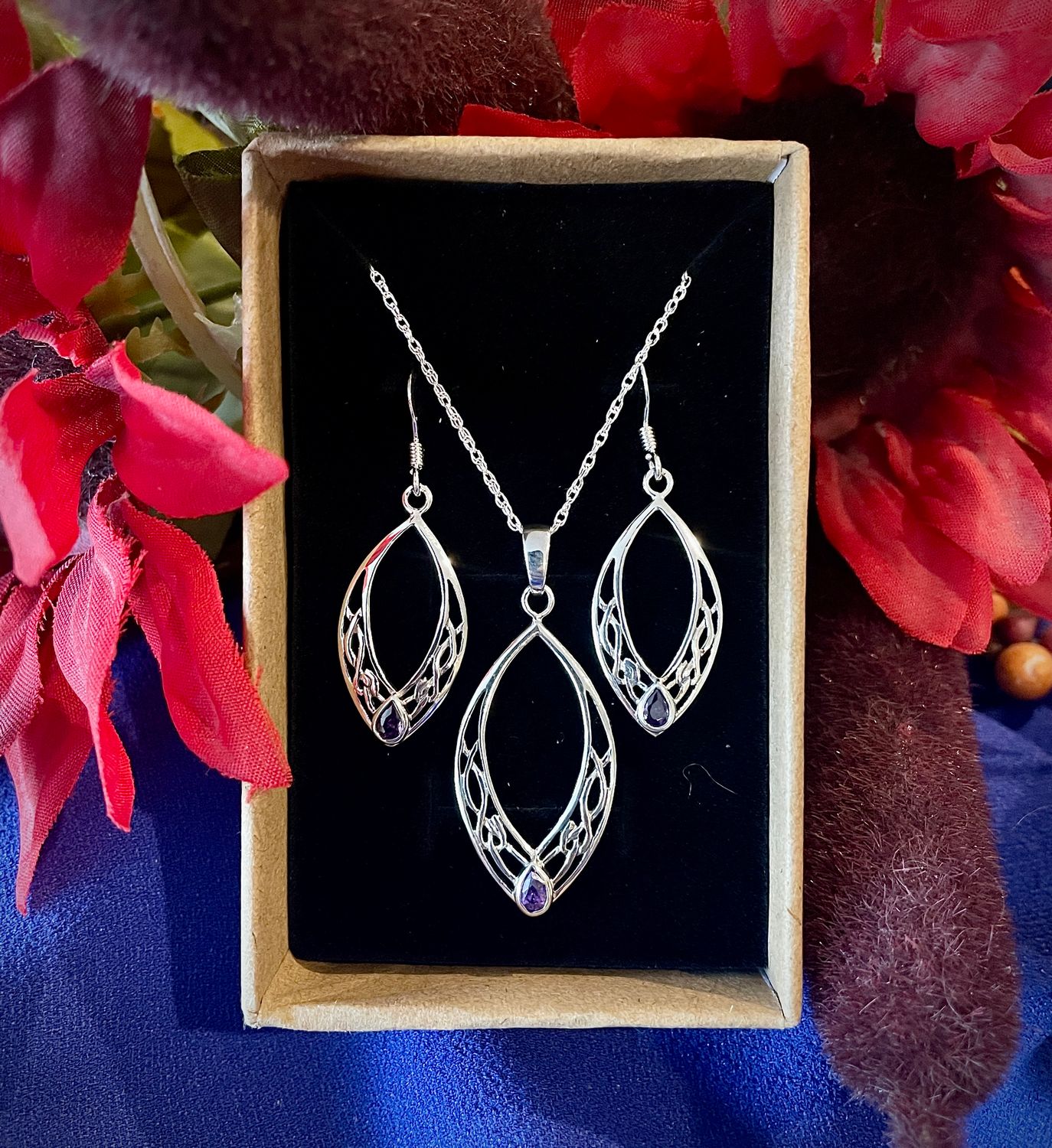 Sterling Silver Oval Celtic Knot Scottish pendant and earrings, with amethyst colored gemstone, in jewelry box near flowers.