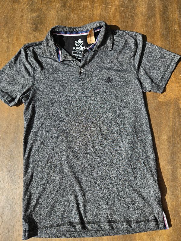 REMERA DE ALGODÓN, CON CUELLO TIPO POLO, MANGA CORTA, COLOR GRIS MELANGE, MARCA RUGBY. TALLE S