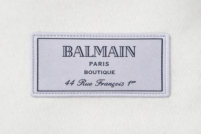 Close-up of Balmain Paris Boutique logo patch on luxury men’s white cotton T-shirt
