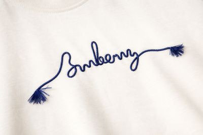 Burberry blue embroidered logo detail on cream luxury mens t shirt fabric close up