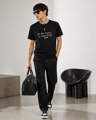 saint laurent black embroidered t shirt men's walking pose with bag studio lifestyle look