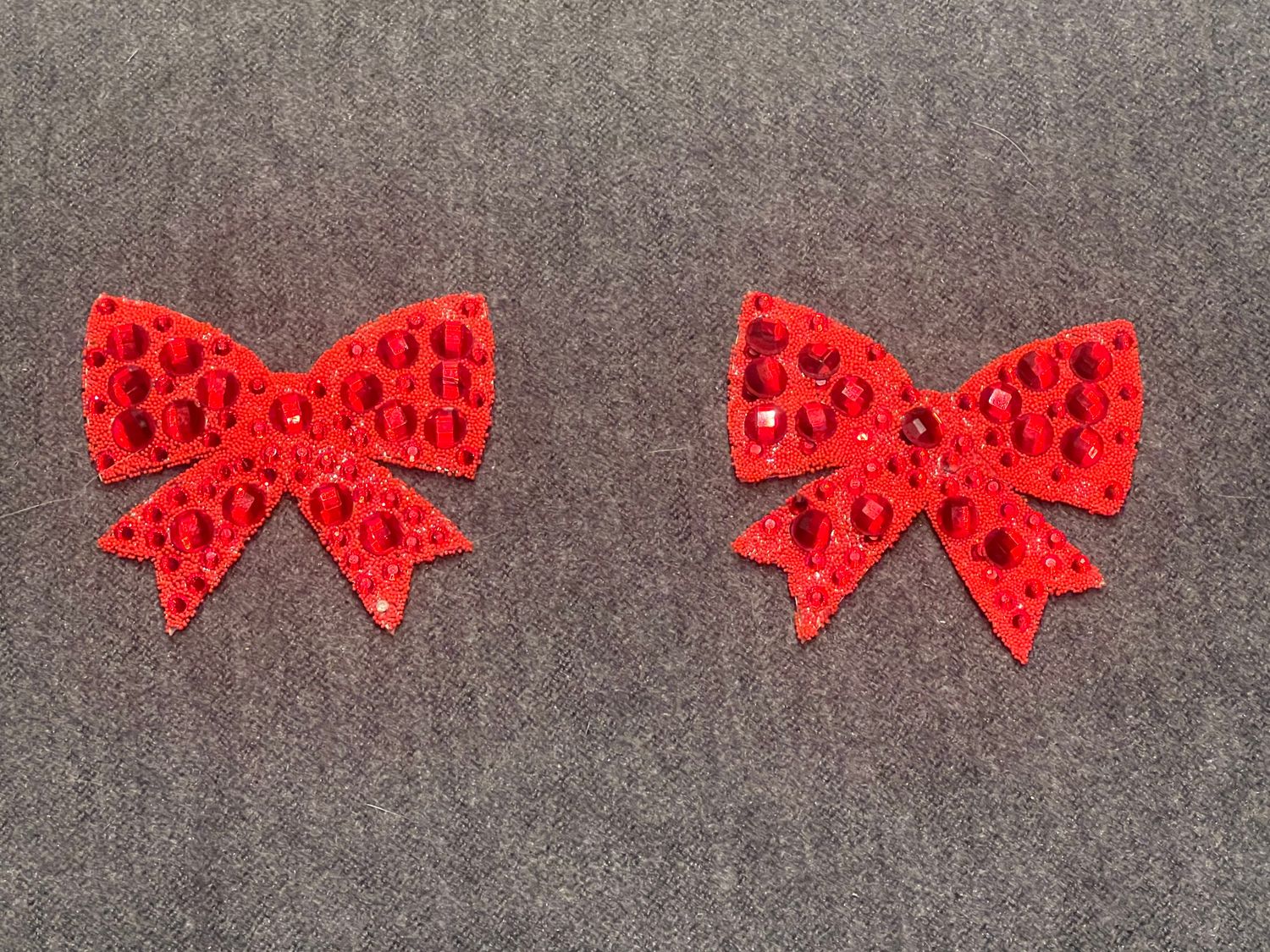 2 rote Schleifen-Nipplepads aus Gummi und mit Glassteinen.