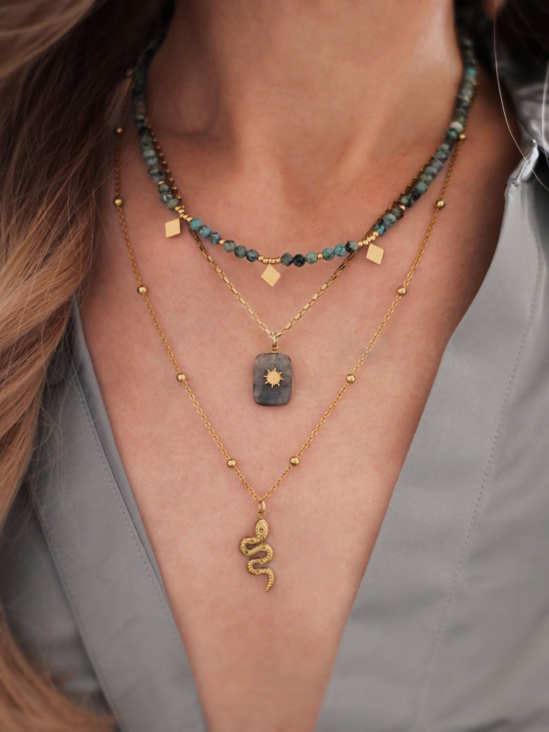 Zarte, goldene Halskette mit Perlen verziert, an der ein Schlangen-Anhänger hängt. Hübscher Boho-Schmuck mit Symbolkraft