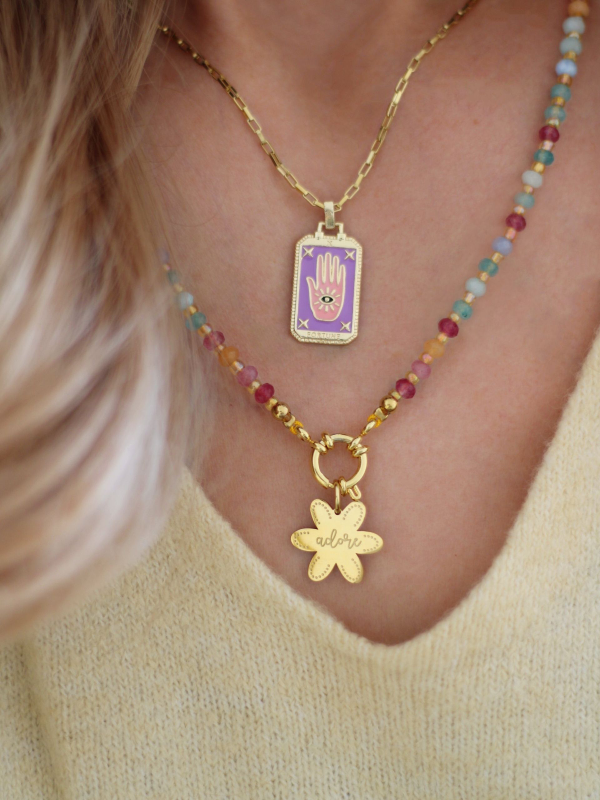 Zarte goldene Halskette mit farbigem Anhänger in rechteckiger Form, der verziert ist mit einer Hand mit Auge in Violett Rosa