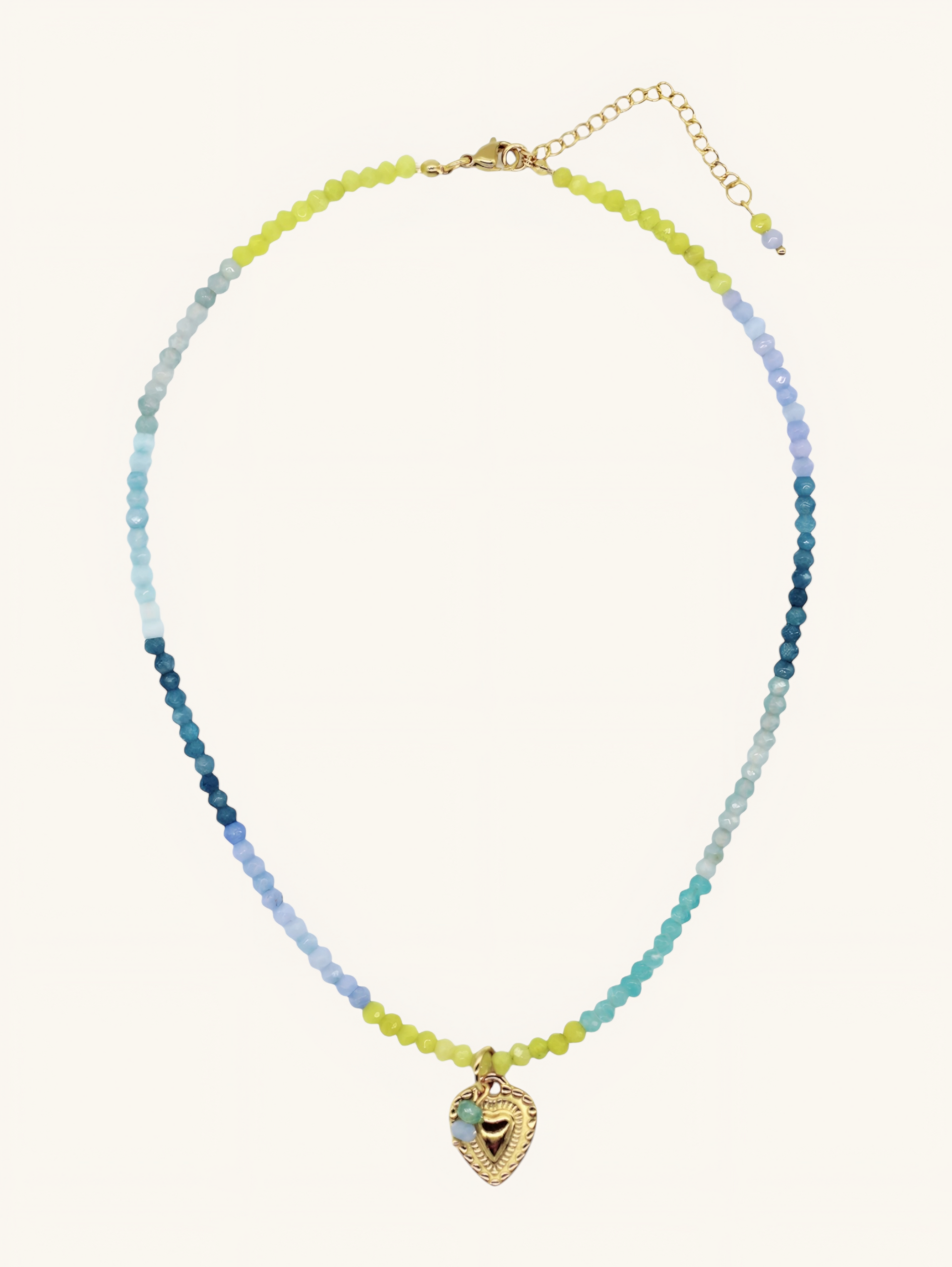 Handgemachte Halskette in Blau-Türkis aus Halbedelsteinen mit goldenem Herzanhänger getragen mit einer Leo-Bluse