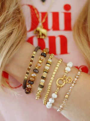 Mehrere funkelnde Armbänder aus braunen, goldenen und weißen Perlen am Arm getragen, Trendschmuck 2025