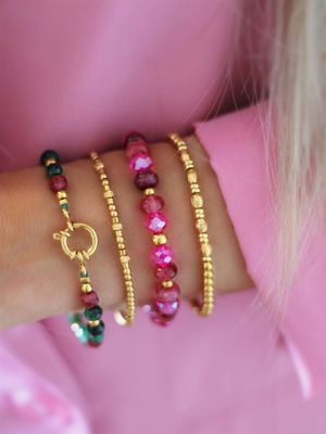 Funkelnde Armbänder aus goldenen und Pinken Perlen im Layering am Arm getragen. Ausgefallener Boho-Chic und Trend 2025