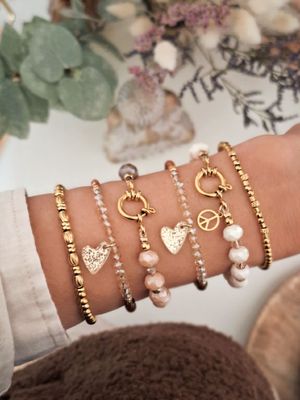 Mehrere funkelnde Armbänder aus braunen, goldenen und weißen Perlen am Arm getragen, Trendschmuck 2025