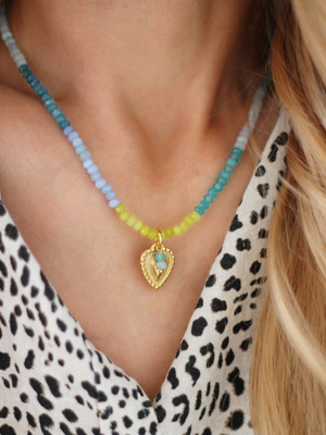 ENYA Boho Halskette mit Halbedelsteinen & Herzanhänger in Blau-Türkis – Bunter Schmuck Handgemachte Halskette in Blau-Türkis aus Halbedelsteinen mit goldenem Herzanhänger getragen mit einer Leo-Bluse