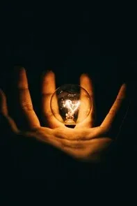 ampoule électrique allumée qui éclaire, dans le noir, une main grande ouverte. Illustration d&#39;un article de blog qui vise à éclairer mes consultant.e.s sur les conditions d&#39;une voyance mail réussie !