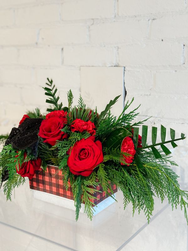 Compact Christmas table centrepiece with red roses, festive greenery and a decorative checked vase