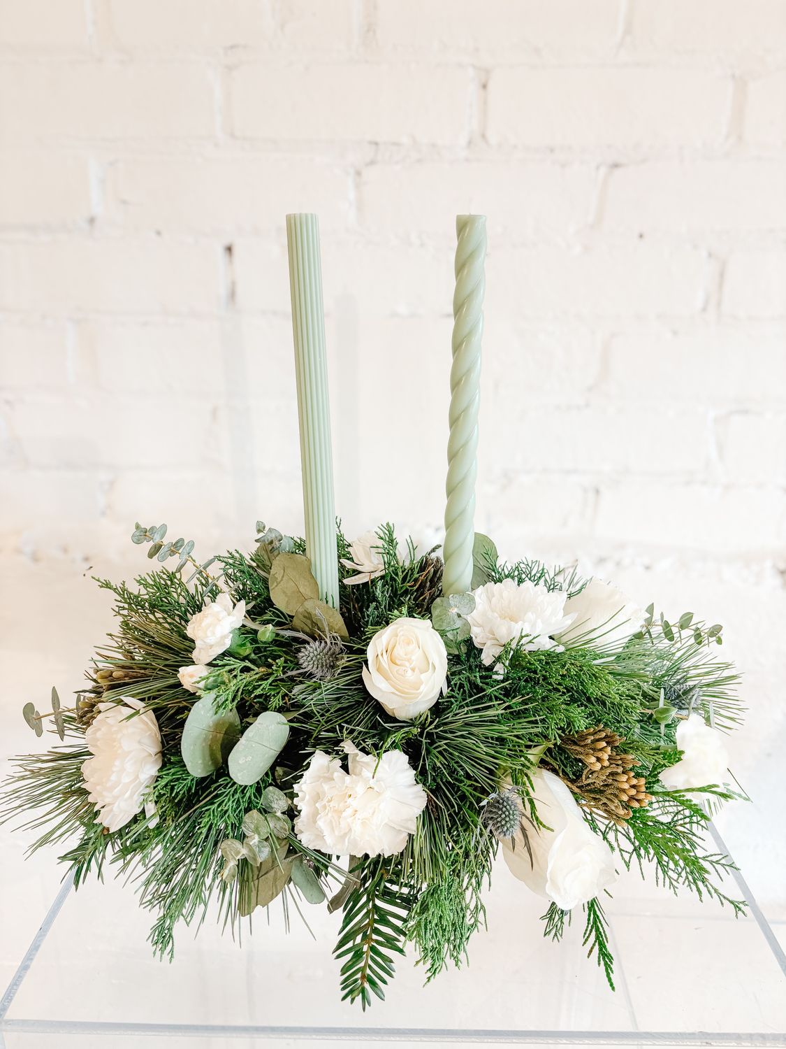 Traditional white Christmas centrepiece with taper candles, white flowers and evergreen greenery