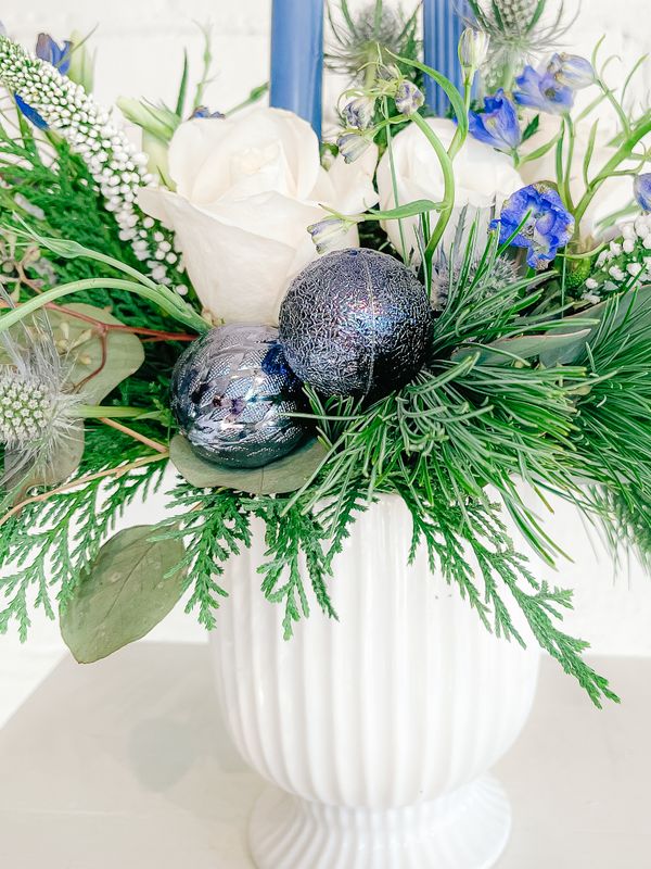 Close-up of blue thistle, white roses, winter greenery and blue accents in a Christmas floral arrangement