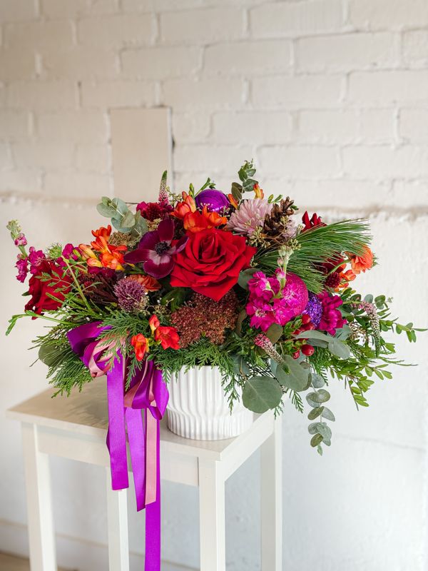 Holiday Bright colourful Christmas flower arrangement with pink, red and purple blooms in a white vase