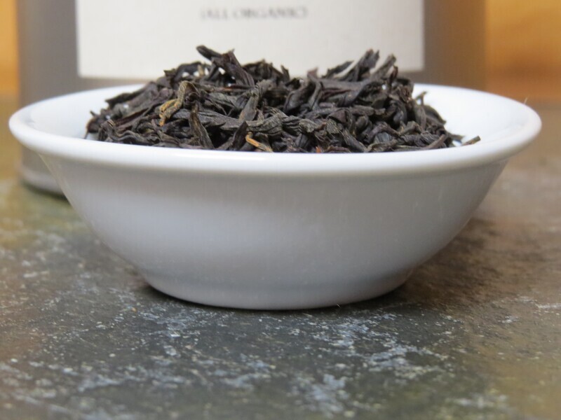 A small white bowl on a stone tabletop, filled with a blend of black and golden teas. Behind it can be seen the barest edge of a label.
