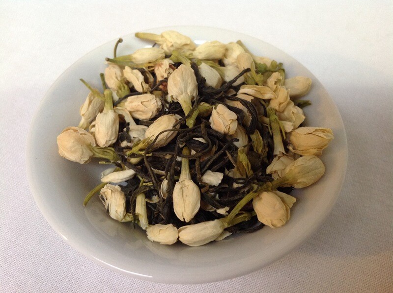 A small white bowl, edges made distinct from the white background by sharp shadows, filled with a blend of green tea and jasmine flowers.