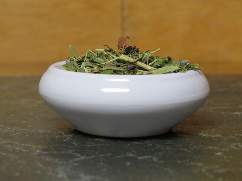 A small white bowl, viewed from the size, filled full enough of a blend of herbs and flowers that it mounds up and can be seen.