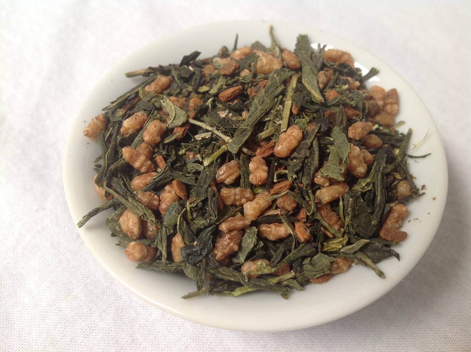 A small white bowl filled with a blend of green tea, roasted rice, and a dusting of nutmeg.