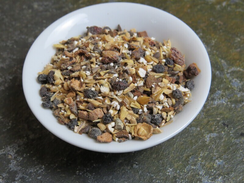 A small white bowl on a green stone surface, filled with a blend of barleys, hawthorn berries, and spices.