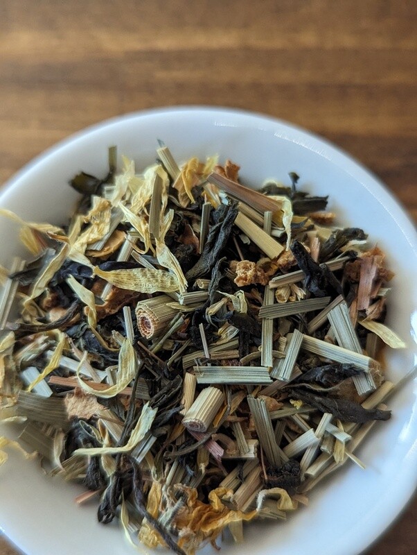 A blend of green tea, lemongrass, lemon peel, and calendula flowers fills a small white bowl and most of the image, as it is zoomed in very close.